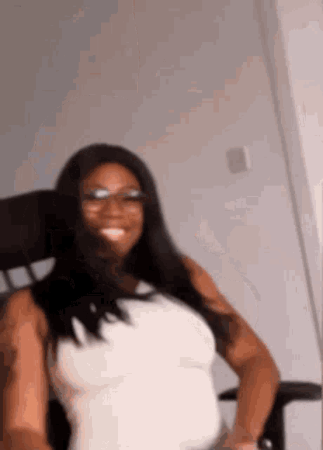 a woman wearing glasses and a white tank top is sitting in an office chair .