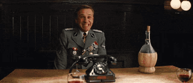 a man in a military uniform is sitting at a table with a telephone and a bottle of wine