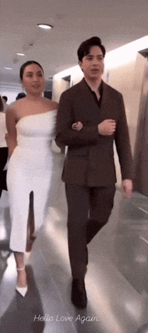 a man in a suit and a woman in a white dress walk down a hallway