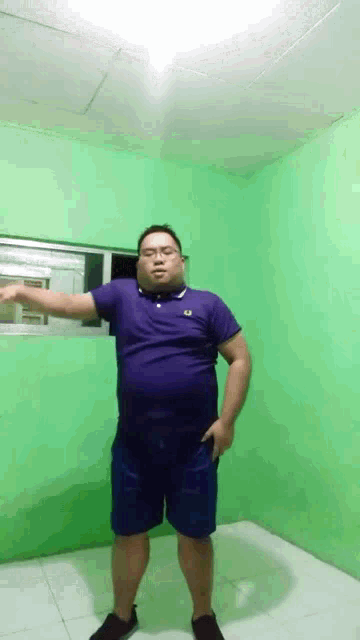 a man in a purple shirt and blue shorts is standing in front of a green wall .