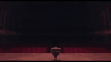 a cartoon character is standing on a stage in a large empty auditorium .