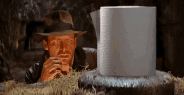 a man in a fedora is looking at a roll of toilet paper