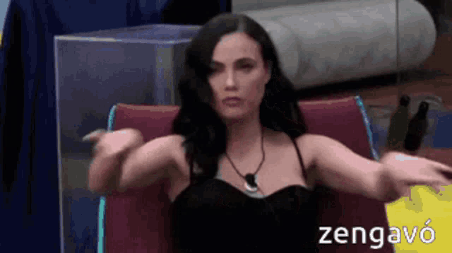 a woman in a black dress is sitting in a chair with her arms outstretched in front of a sign that says zengavo