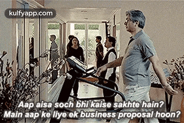 a man is walking on a treadmill in a hallway while a group of people are standing in the background .