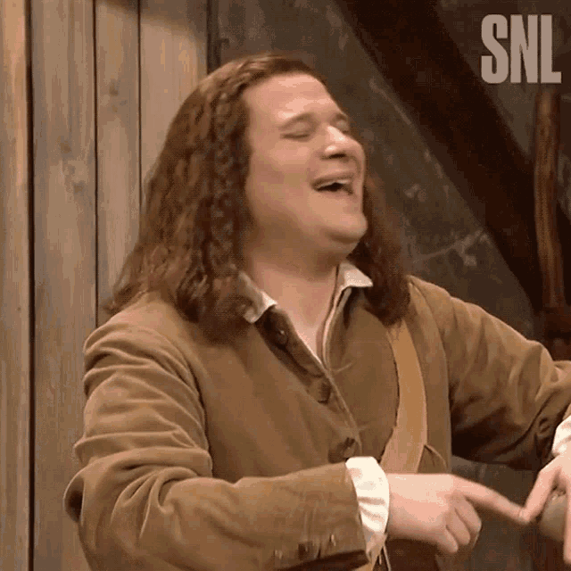 a man with long hair is laughing in front of a wall that says sni