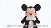 a mickey mouse mascot is wearing a black jacket and red pants and has his arms outstretched .