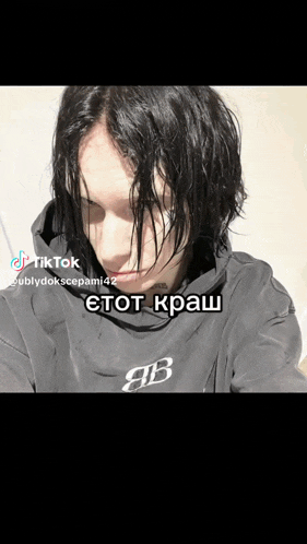 a man with black hair is wearing a black hoodie with a b on it