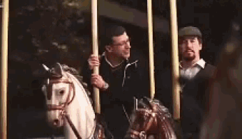 two men are riding horses on a merry go round at a park .