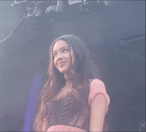 a woman in a pink dress is standing on a stage with her hand on her hair .