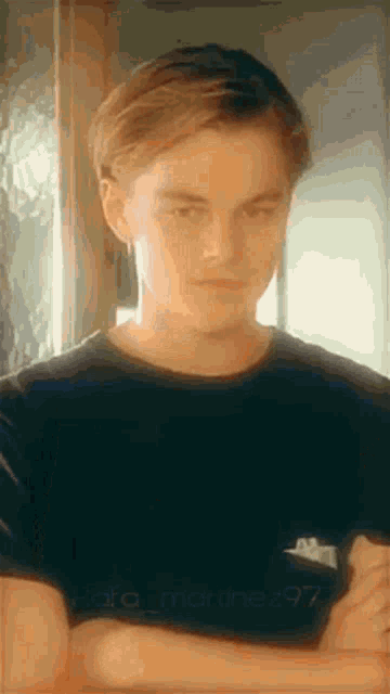 a young man with his arms crossed is wearing a black t-shirt .