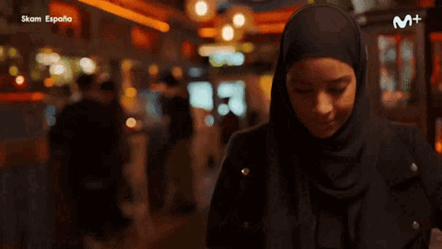 a woman wearing a hijab is looking at her phone with a help search bar