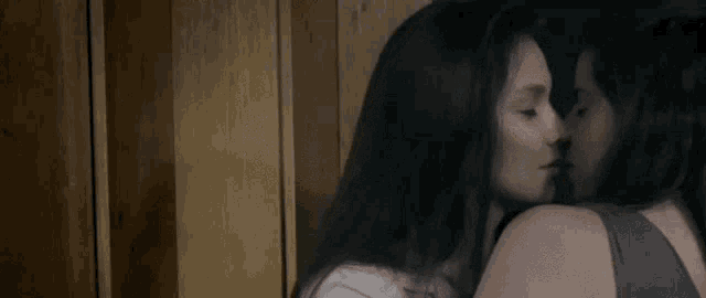 a couple of women are kissing each other in front of a wooden wall .