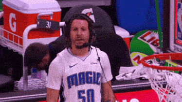 a man wearing headphones and a magic 50 jersey stands in front of a gatorade cooler