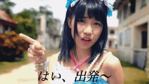 a girl in a blue dress is pointing at something with chinese writing behind her