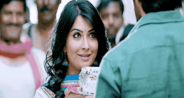 a woman is smiling while holding a cake in front of a man in a green jacket