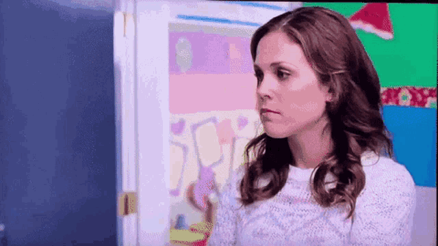 a woman in a white sweater is standing in front of a colorful wall