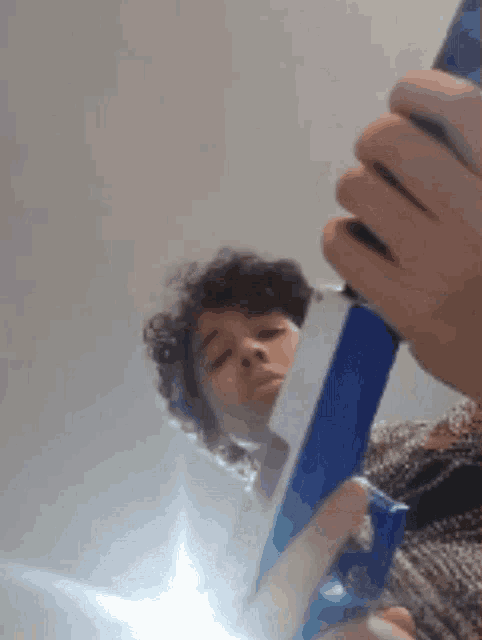 a person with curly hair is holding a blue object in their hand