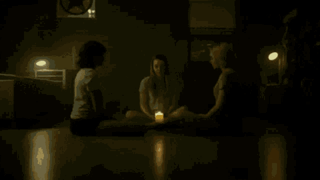 three women sit in a circle holding a candle