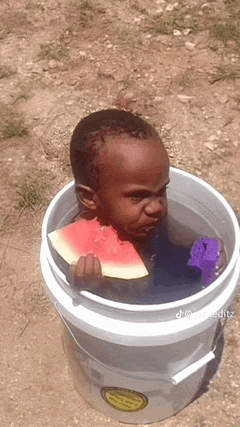 a young boy is sitting in a bucket of water eating a slice of watermelon .