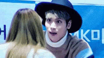 a man wearing a hat and a turtleneck is talking to a woman