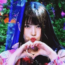a woman making a heart with her hands in front of a christmas tree