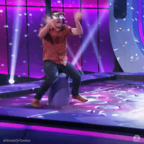 a man is sitting on a barrel on a stage with his arms in the air