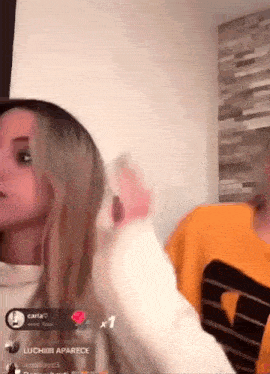two women are standing next to each other in a living room and one of them is wearing a yellow shirt with the letter d on it .