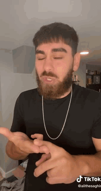 a man with a beard is wearing a black shirt and a chain around his neck