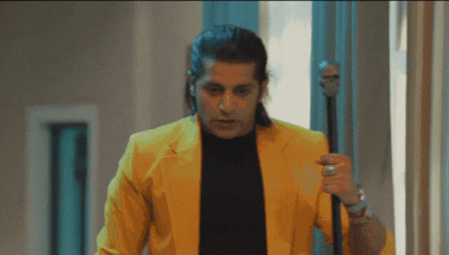 a man in a yellow jacket and black shirt holds a cane