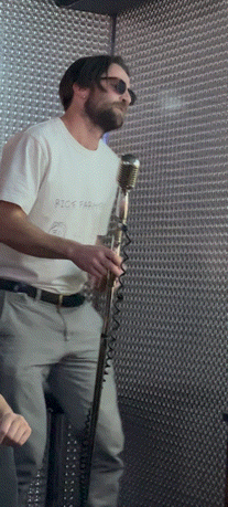 a man singing into a microphone wearing a white shirt that says rick farm