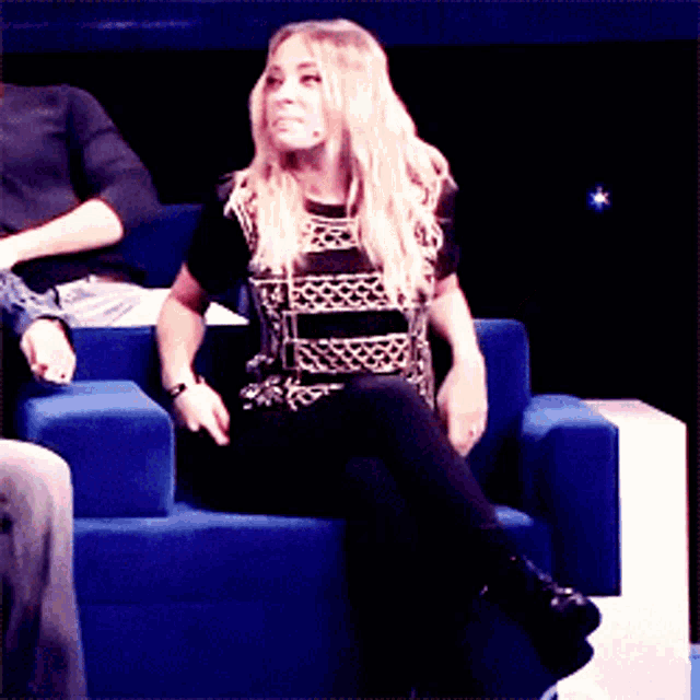 a woman sits on a blue couch with a microphone in her hand