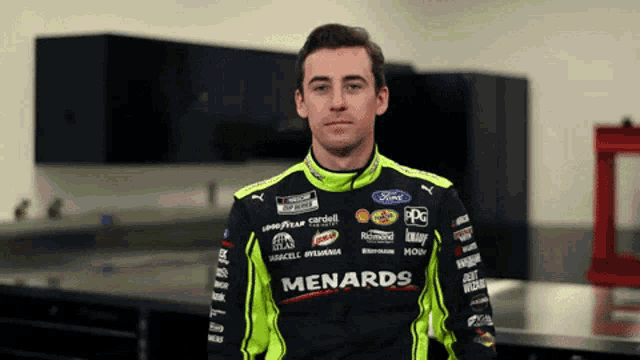 a man in a menards racing suit stands in a room