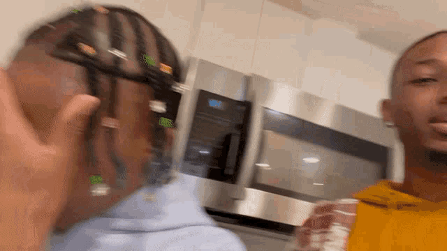 two men are standing in front of a microwave and one has dreadlocks on his head .