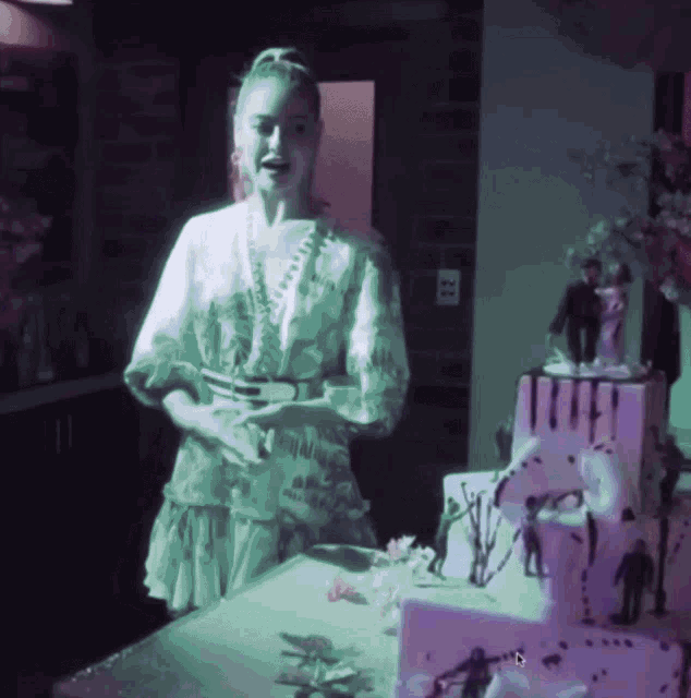 a woman stands in front of a cake with a bride and groom on top