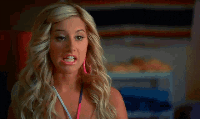 a woman with blonde hair and pink and blue earrings looks at the camera