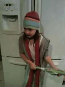 a little girl wearing a hat and scarf stands in front of a fridge