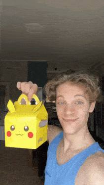 a young man in a blue tank top is holding a yellow box with a pikachu face on it