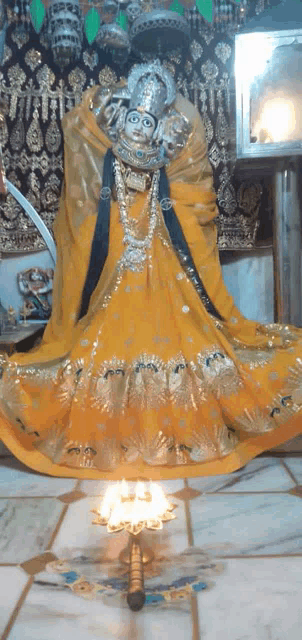 a statue of a woman in a yellow dress with a candle in front of her