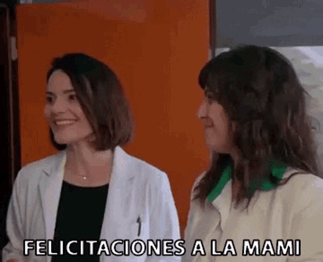two women in lab coats are standing next to each other in a room and smiling .