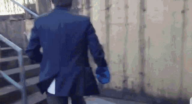 a man in a blue jacket is walking down stairs holding a blue glove