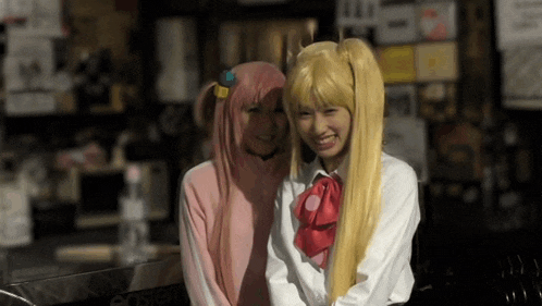 two girls are posing for a picture with one wearing a pink sweater and the other wearing a blonde wig
