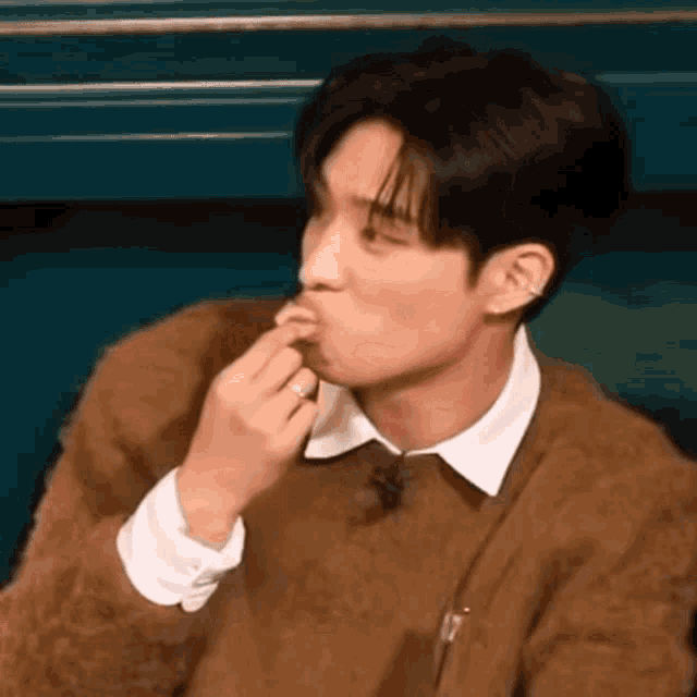 a man wearing a brown sweater and a white shirt is eating a piece of food .