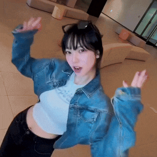 a woman wearing a denim jacket and a white t-shirt is standing in a hallway with her arms outstretched