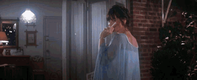 a woman in a blue dress is smoking a cigarette in front of a brick wall