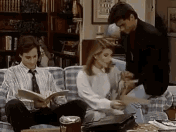 a man and a woman are sitting on a couch reading books .