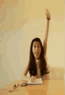 a woman sitting at a table with her arm in the air .