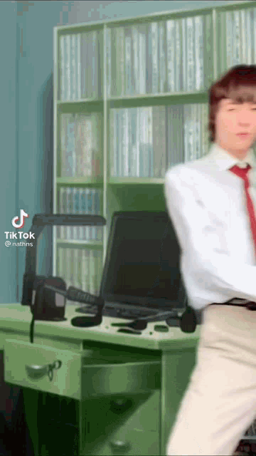 a man in a white shirt and red tie is dancing in front of a desk with a computer .