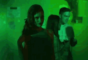 a group of people are dancing in a dark room with green lights behind them .