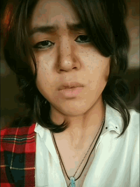 a woman wearing a plaid shirt and a necklace is making a sad face