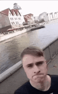 a man is taking a selfie in front of a body of water with buildings in the background .